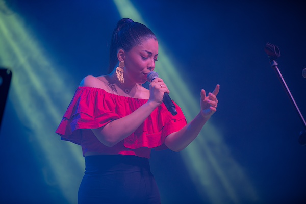 Lucía singing into a microphone in a red shirt